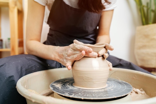 Muddy hands of a young woman shaping clay on a pottery wheel in a workshop