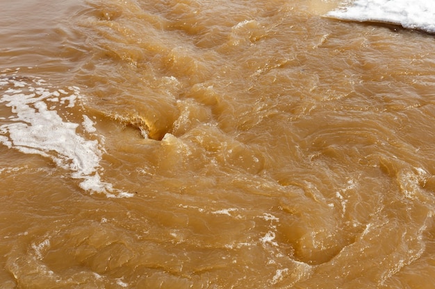 Muddy river water spring flood dirty muddy water with whirlpool and white foam closeup