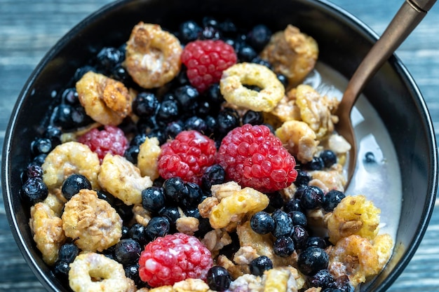 Muesli with raspberries blueberries and flakes in a black bowl Healthy food healthy breakfast concept