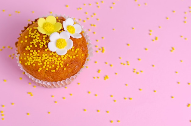 Muffin decorated with flowers on pastel pink background.