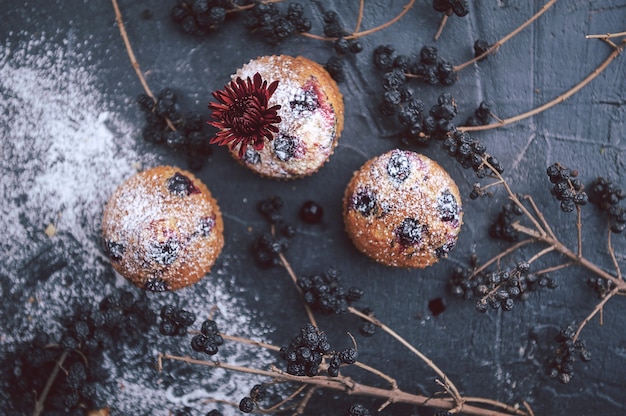 Muffin with currants on a dark background next to the berries on the branches. and a bouquet of flowers. in a rustic style. dark style