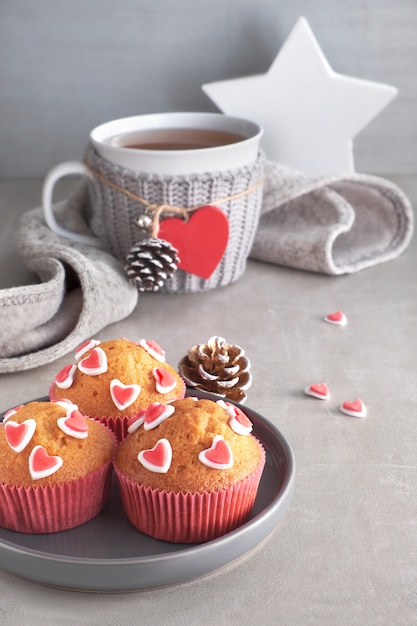 Muffins decorated with sugar hearts and a cup with red heart on light gray background