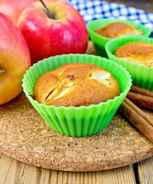 Muffins with apples in silicone molds, cinnamon, napkin on a wooden boards background