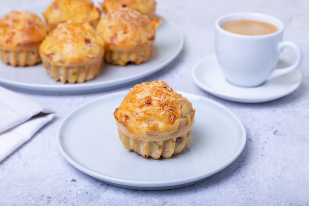 Muffins with ham and cheese. Homemade baking. In the background is a plate with muffins and a cup of coffee. Close-up.