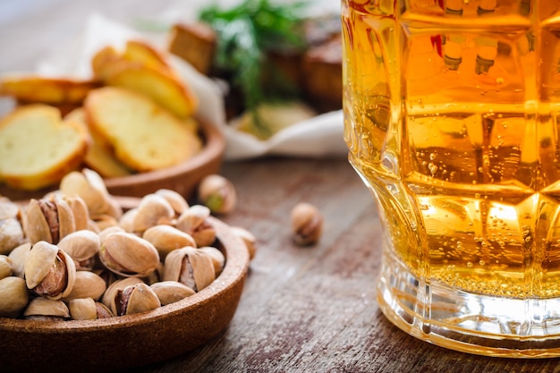 A mug of beer and salted pistachios on a wooden table