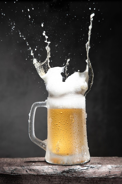 Mug of beer with foam and splashes on wooden table isolated on dark background. Vertical format.