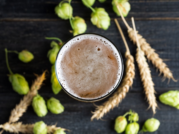 A mug of beer on a wooden table with green hops and ears of wheat 