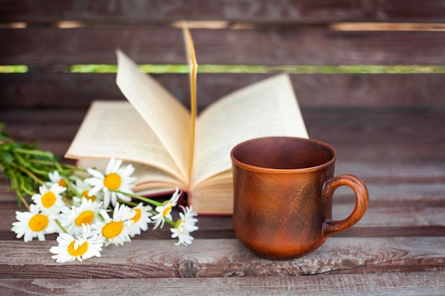 mug bouquet of daisies and open book on wooden background