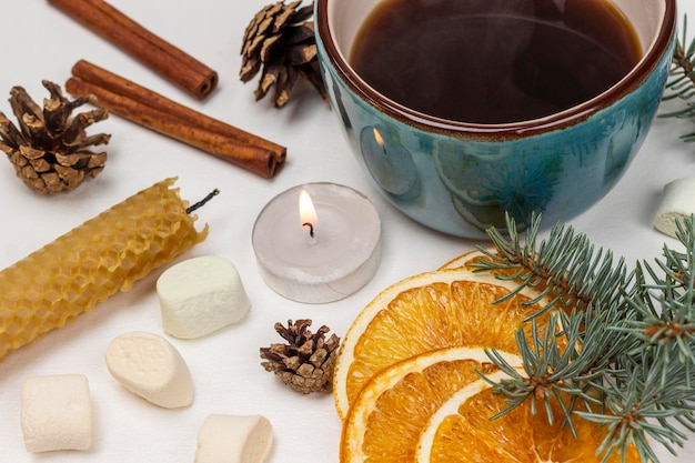 A mug of coffee a lit candle a spruce branch cones and dry orange slices