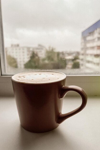 A mug of coffee stands on the windowsill on a cloudy rainy day