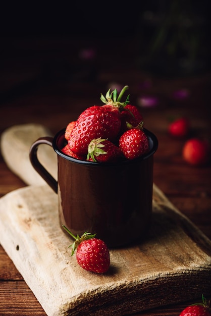 Mug full of fresh strawberries on rustic table