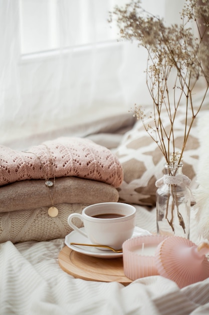 A mug of hot cocoa, knitted sweaters, a bouquet of white dried flowers in a vase, a candle on the bed. Breakfast in bed. Cozy. Spring.