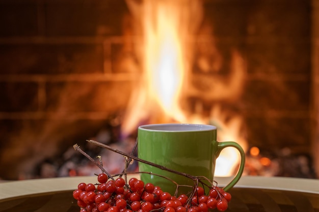 Mug of tea and a bunch of viburnum berries by a cozy fireplace in a country house