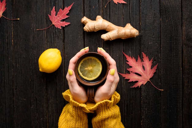 Mug of tea in female hands Lemon ginger and autumn leaves Cold treatment Wooden background Top view