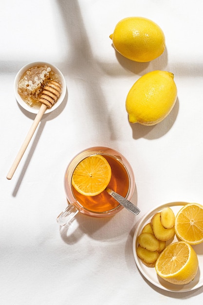 A mug of tea with lemon and a plate of honey with a wooden spoon on a table covered with a white tab