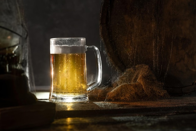 Mug with fresh light beer with foam on wooden vintage background with barrelÑ Old wine cellar or pub