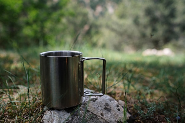 A mug with a hot drink stands on a stone in nature