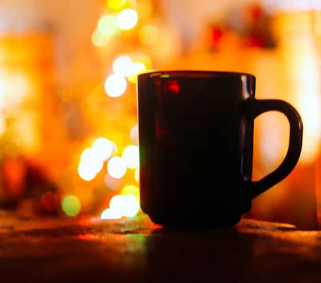 A mug with hot tea on colorful Christmas decorations close up.