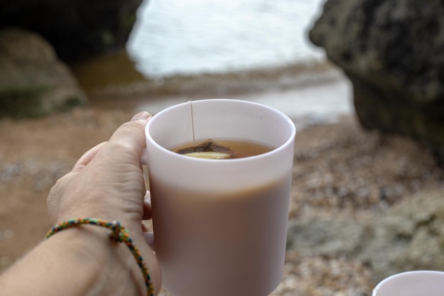 A mug with tea in the hand of a tourist overlooking the sea rocky shore Travel and tourism