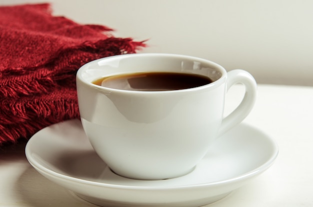 Mug with warm tea on a white table with a red folded warm blanket.