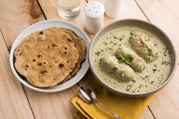 Mughlai Or Haryanvi style Methi Malai Kofta in white cream, popular indian vegetarian main course served in wooden bowl with Chapati Or Roti, selective focus