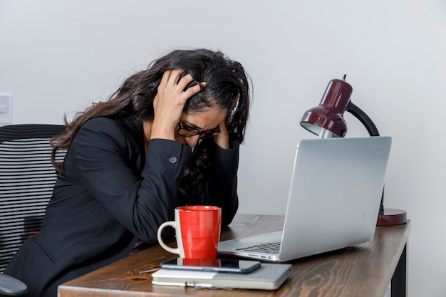 Mujer ejecutiva cansada por el exceso de trabajo en casa se lleva las manos a la cabeza