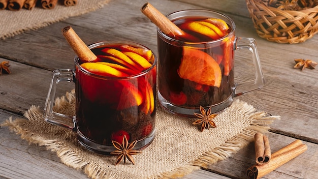 Mulled wine in glass mugs with spices and citrus fruit on an old wooden table