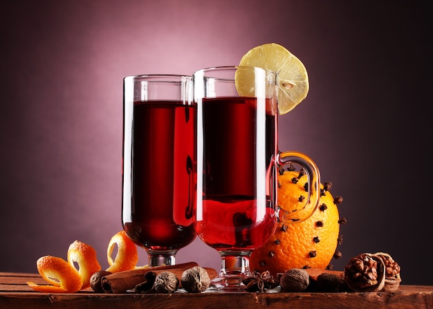 Mulled wine in the glasses, spice and orange on wooden table on purple wall