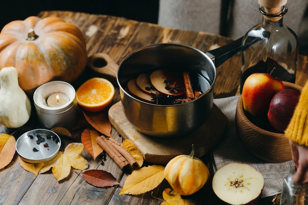 Mulled wine hot drink with citrus, apple and spices in aluminum pot on wood