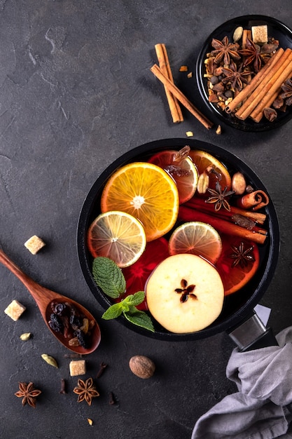 Mulled wine traditional christmas hot drink with citrus, apple and spices in pan. Top view
on black background. Recipe.