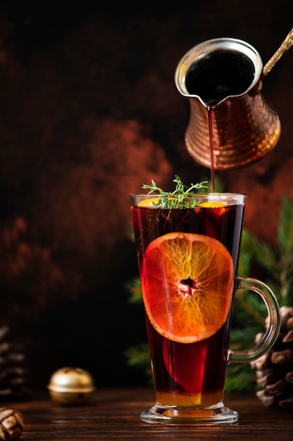 Mulled wine a warm drink made of red wine, citruses and spices in a glass on a wooden table with Christmas decorations. Mulled wine pouring into a glass. Dark background. Copy space. Close-up