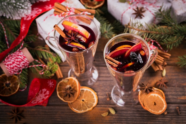 Mulled wine with fruits, cinnamon sticks, anise, decorations and gift boxes on dark wooden  background. Winter warming drink with recipe ingredients.