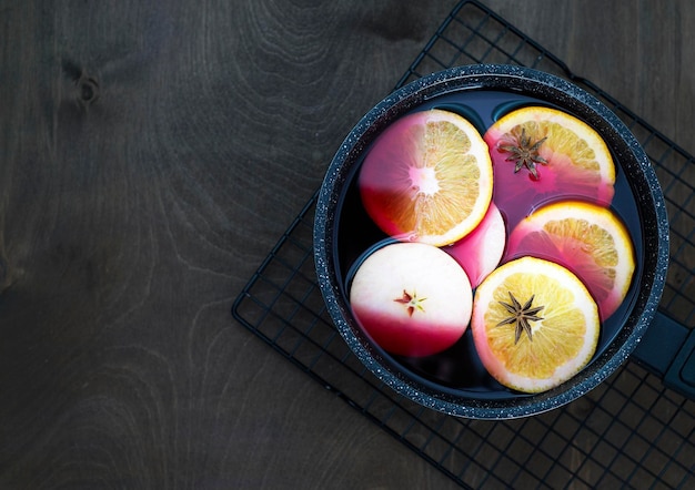 Mulled wine with pieces of oranges and apples in a black ladle on a wooden background