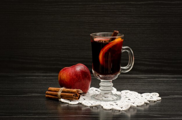 Mulled wine with spices on a lace napkin, apple and cinnamon sticks. Black wood 