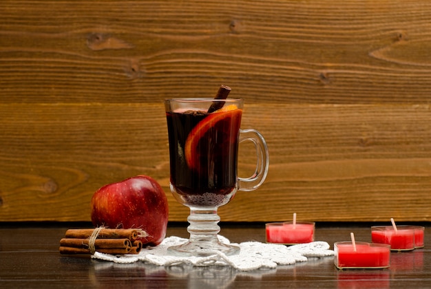 Mulled wine with spices on a lace napkin. Candles in the shape of a heart, cinnamon sticks and apple.