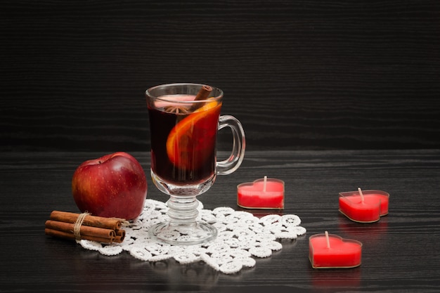 Mulled wine with spices on a lace napkin. Candles in the shape of a heart, cinnamon sticks and apple.