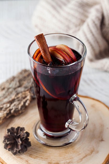 Mulled wine with a stick of cinnamon, spices in a glass on a wooden stand with a knitted jacket in the surface