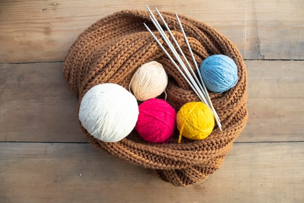 Multi-colored balls of yarn, knitting needles and a knitted product on a wooden table.