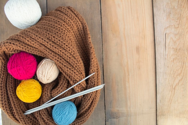 Multi-colored balls of yarn, knitting needles and a knitted product on a wooden table.