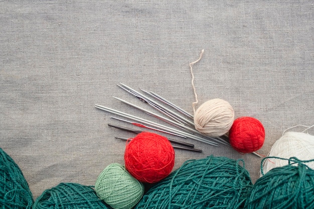 Multi-colored balls of yarn, metal knitting needles and crochet hooks lie on a gray tablecloth.