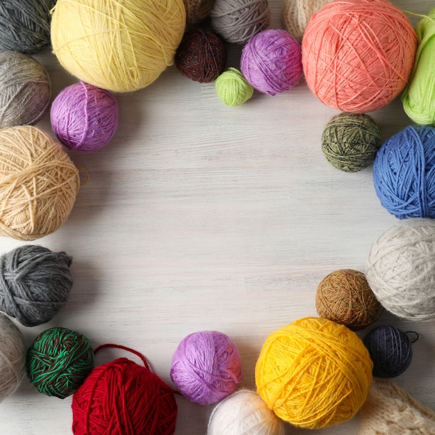 Multi colored balls of yarn on white wooden background.