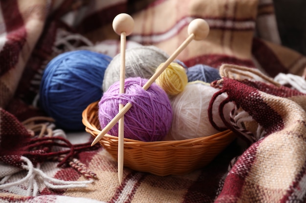 Multi colored balls of yarn with knitting needles in a wicker basket on the background of a plaid.