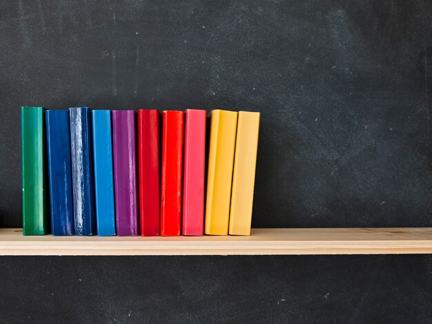 Photo multi colored books on table against blackboard