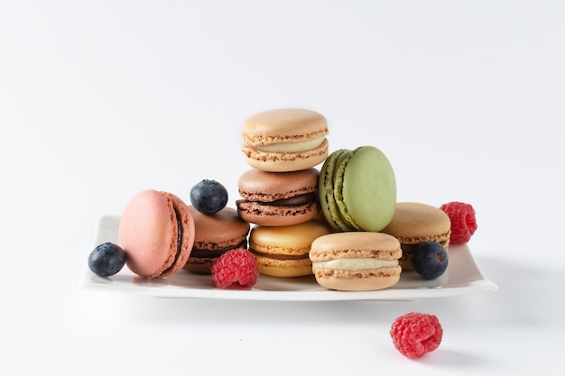 Multi colored french macaroons and berries such as raspberry and blueberry on a plate over white