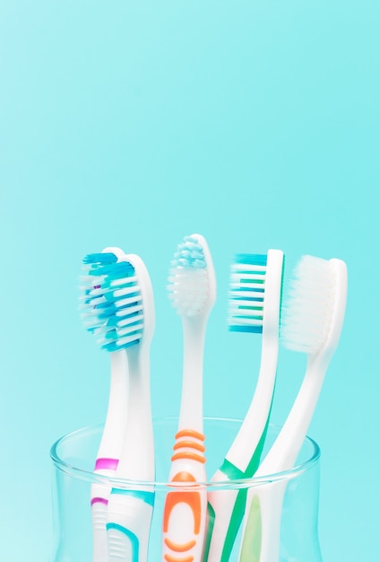 Multi-colored toothbrushes in a glass cup on a blue background