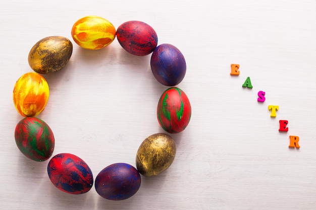 Multi-colored wooden letters making up the words happy easter and decorative colourful eggs on a white background with copy space.