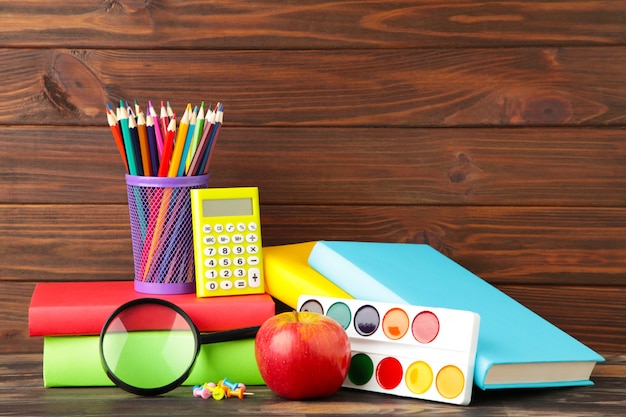 Multi coloured school books and stationery on brown wood