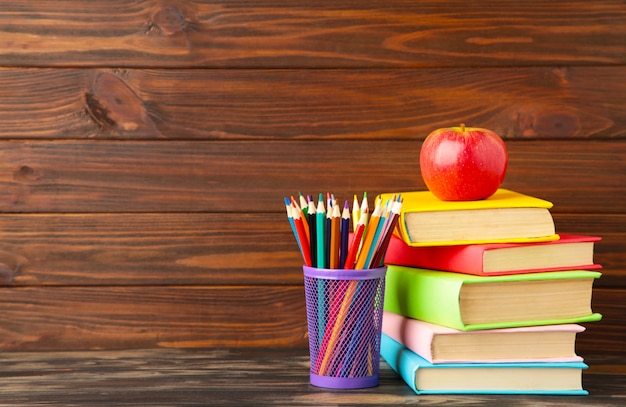 Multi coloured school books and stationery on brown wood