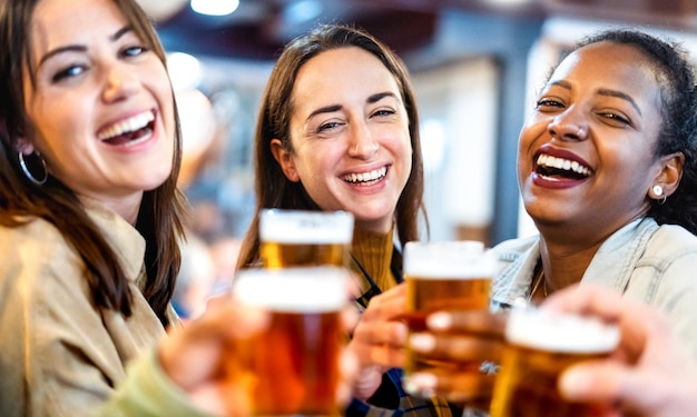 Multi cultural girl friends drinking beer at brewery bar restaurant