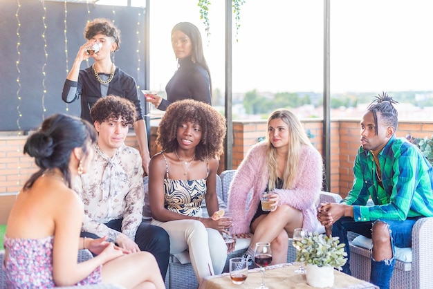 Multi-ethnic friends chatting on a terrace while having a drink at daytime.